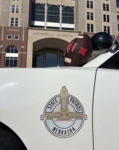 Husker football sitting on a Nebraska State Patrol cruiser outside Memorial Stadium